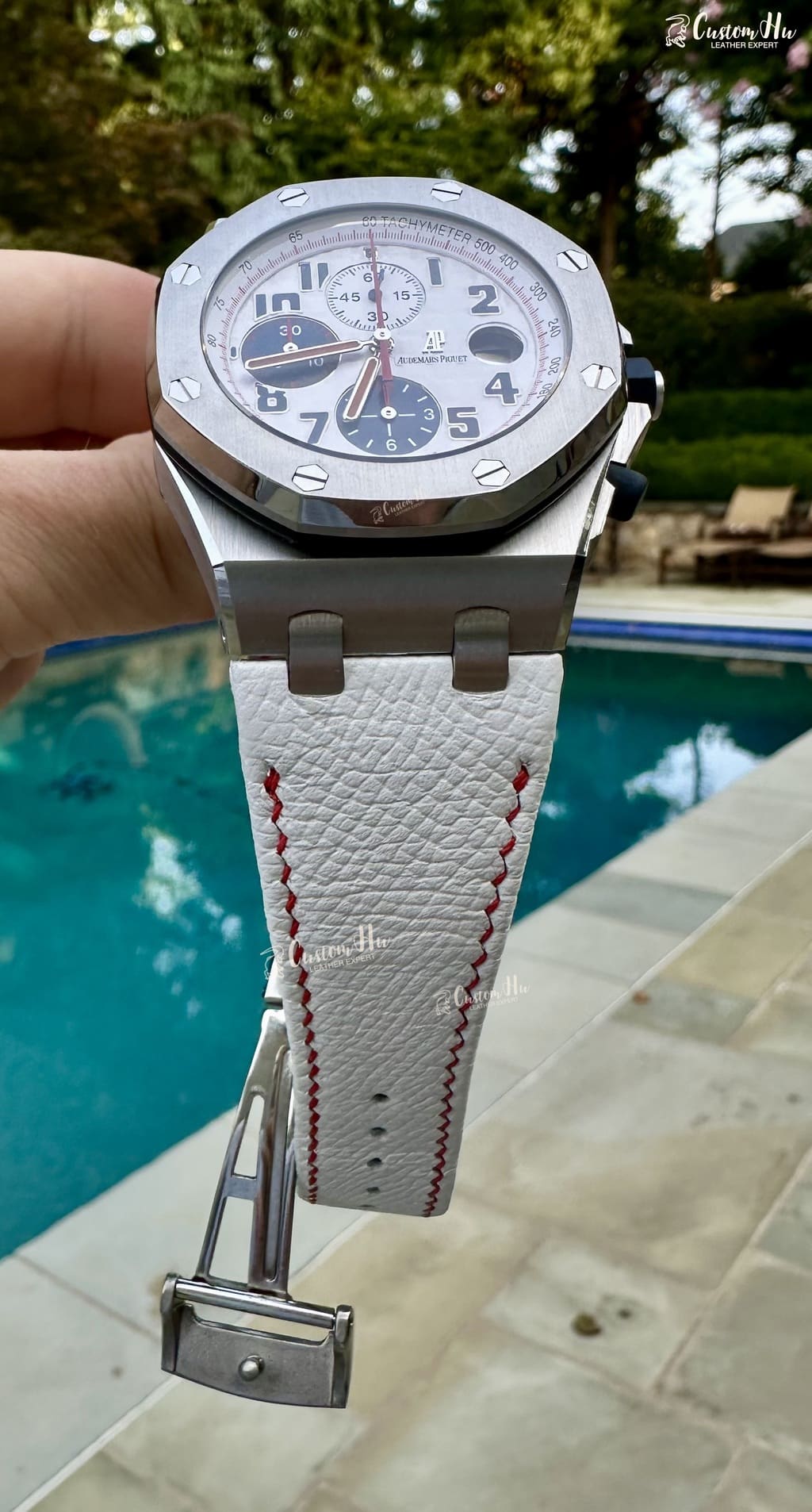 IMG_7641 | CustomHu: Luxury Custom Watch Straps Close-up of a silver Audemars Piguet watch with a white leather strap and red stitching, held above a poolside scene.
